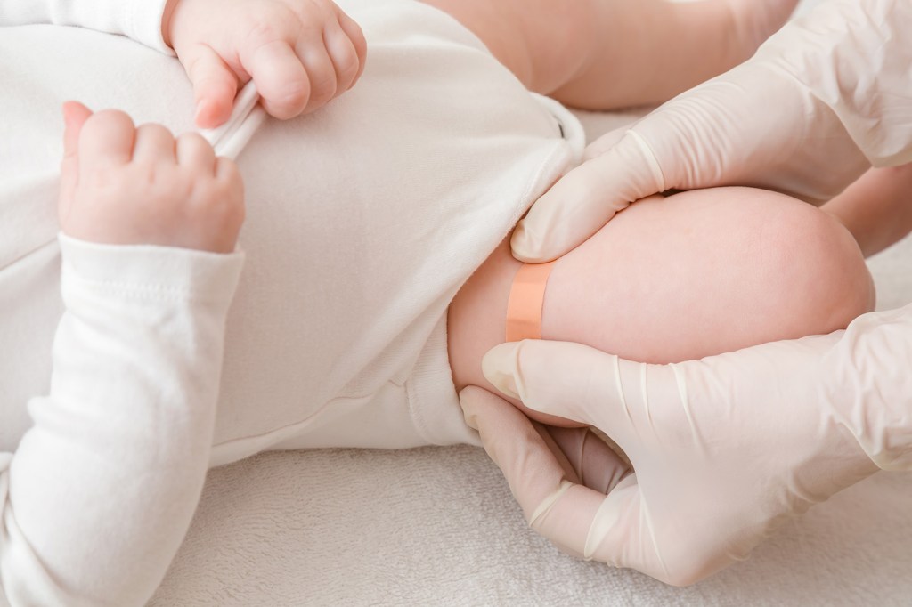 A medical professional puts a Band-Aid on an infant's thigh. 